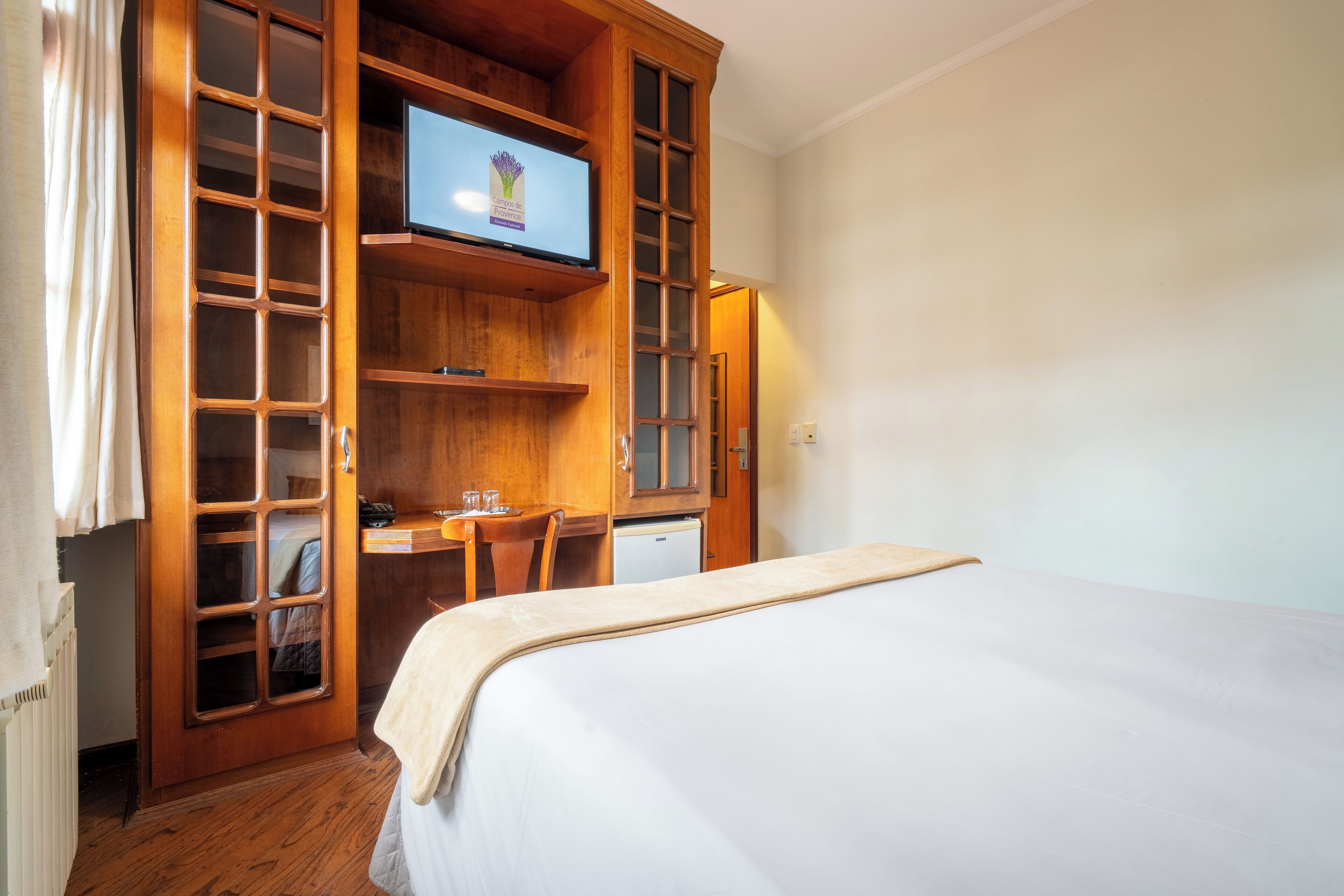 Una habitación de hotel con una cama, un escritorio con una computadora, un televisor y un armario.