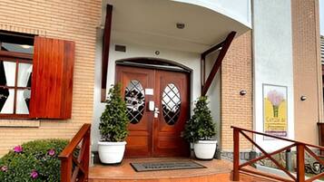 A building entrance with a wooden door, potted plants, and a metal railing.