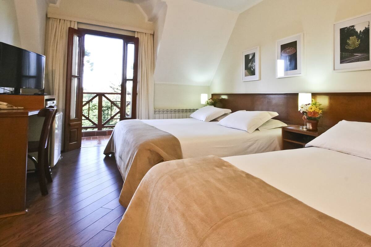 Een hotelkamer met twee bedden, een bureau met een televisie en een balkon met gordijnen.