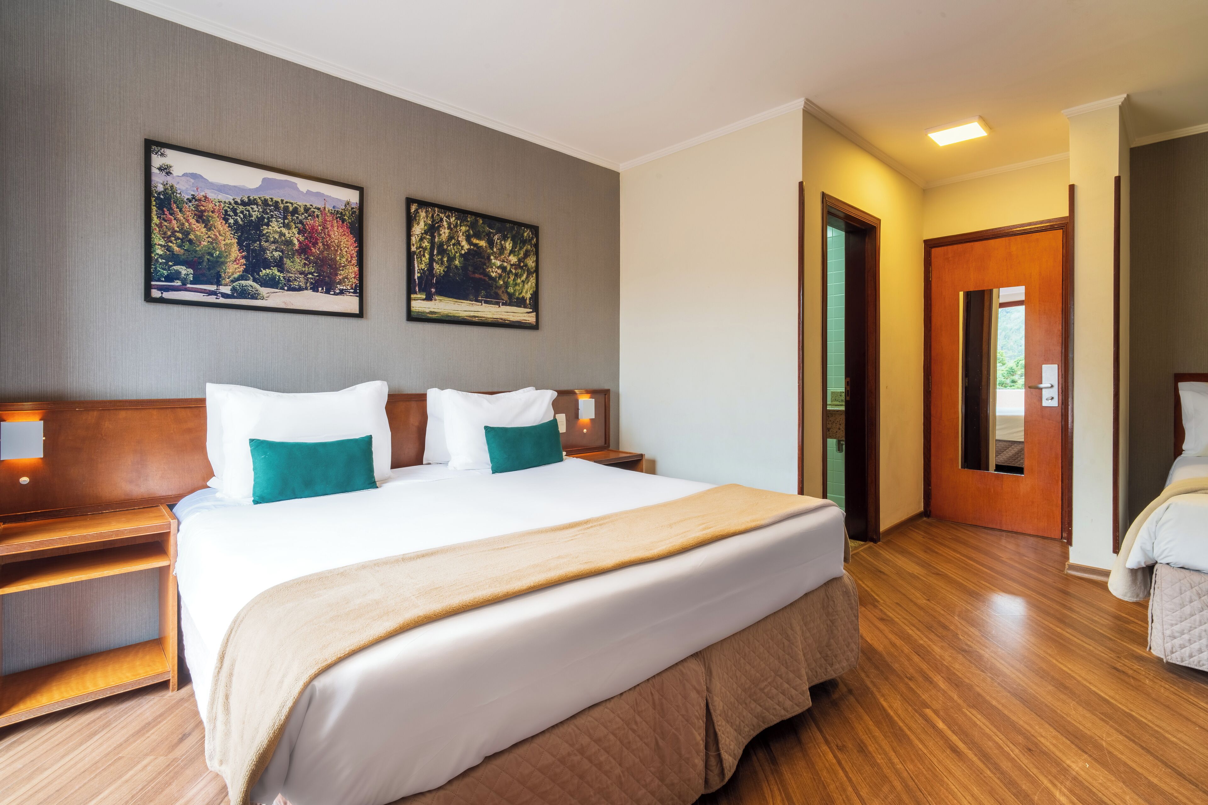 Une chambre d’hôtel avec un grand lit, deux tables de chevet, un plancher en bois et deux tableaux encadrés au mur.