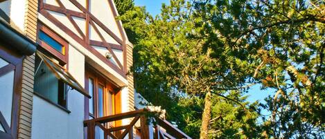 Un bâtiment doté d’un toit à forte pente, d’un balcon avec une balustrade en bois et offrant une vue sur un arbre aux feuilles vertes.