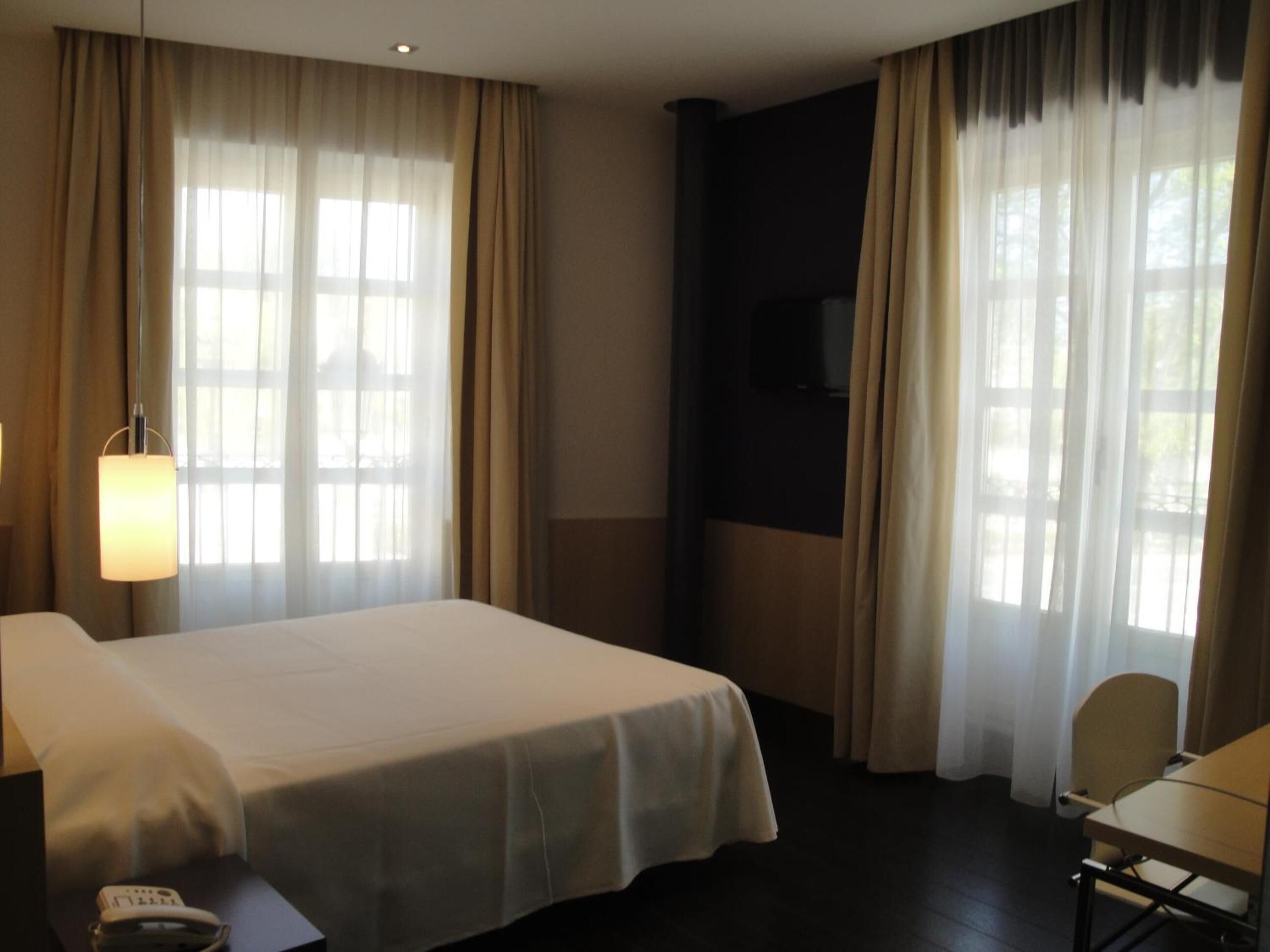 Habitación de hotel con cama, escritorio, silla, lámpara y televisor.