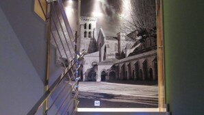 Una escalera con luces LED azules, barandilla de metal y un mural de un edificio en la pared.
