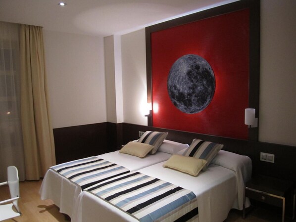 Quarto de hotel com duas camas, um grande mural na parede com a lua e uma janela com cortinas.
