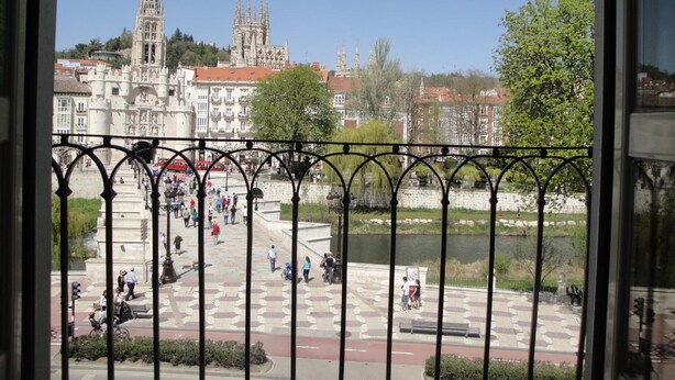 Vista de una plaza con un río, una catedral y gente caminando.