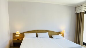 Ein Doppelbett mit weißer Bettwäsche, zwei Nachttische mit Lampen und ein Fenster mit Vorhängen.