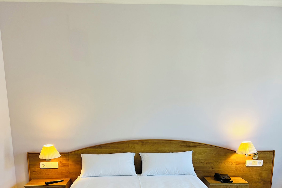 Ein Doppelbett mit weißer Bettwäsche, zwei Nachttische mit Lampen und ein Holz-Kopfteil.
