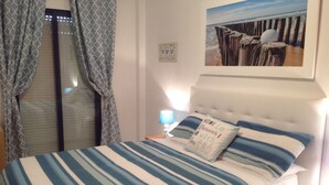 Une chambre à coucher avec un lit recouvert d’une literie à rayures, un oreiller orné d’un motif textuel, un tableau encadré accroché au mur et une fenêtre avec des rideaux.
