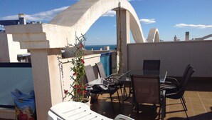 Une terrasse sur le toit avec une table et des chaises, un pot de fleurs et un fauteuil de jardin blanc.