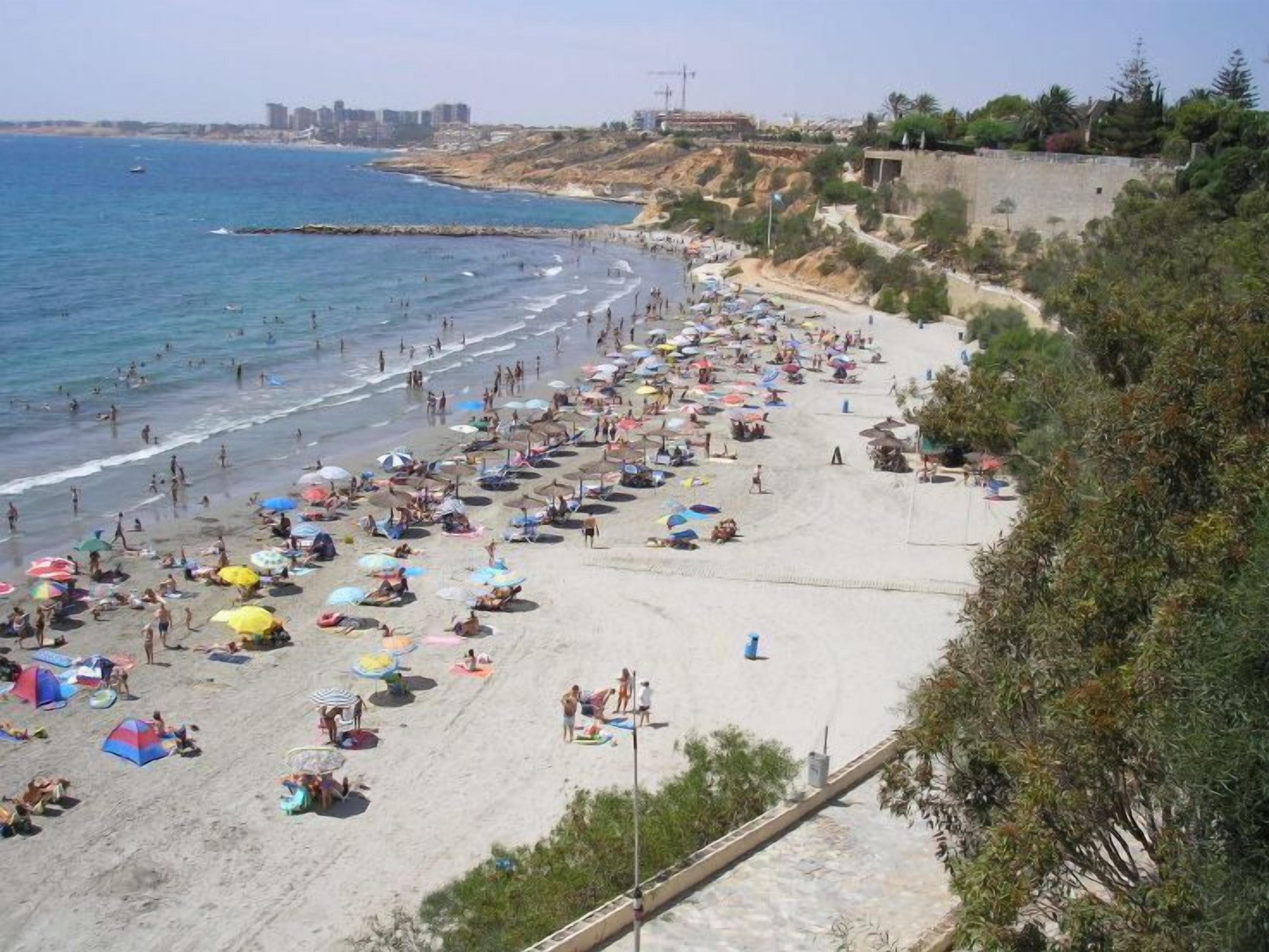 Una playa concurrida, con muchas sombrillas y gente disfrutando del mar.