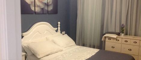 A bedroom with a white bed, a dresser, and a painting of a flower on the wall.