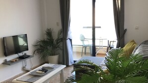 Un salon moderne avec un téléviseur à écran plat, une table basse blanche, un banc et une grande plante en pot.