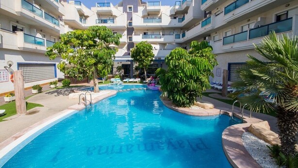Une piscine entourée d’immeubles à plusieurs étages dotés de balcons, d’arbres et de chaises longues.