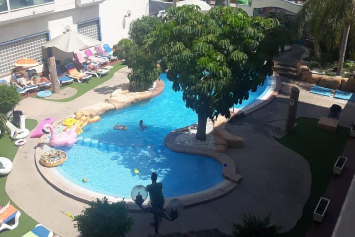 Un área de piscina con sillones de descanso y un árbol.