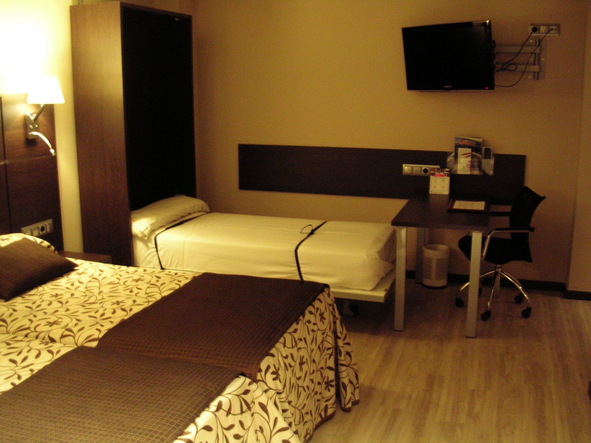 A hotel room with two beds, a desk, a chair, a television, and a coffee machine.
