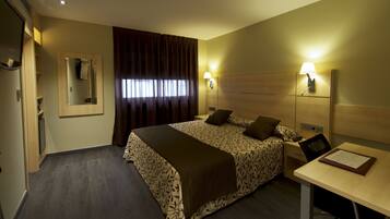 Habitación de hotel con una cama grande, dos mesitas de noche con lámparas, un escritorio, una silla, un espejo y una ventana con cortinas.