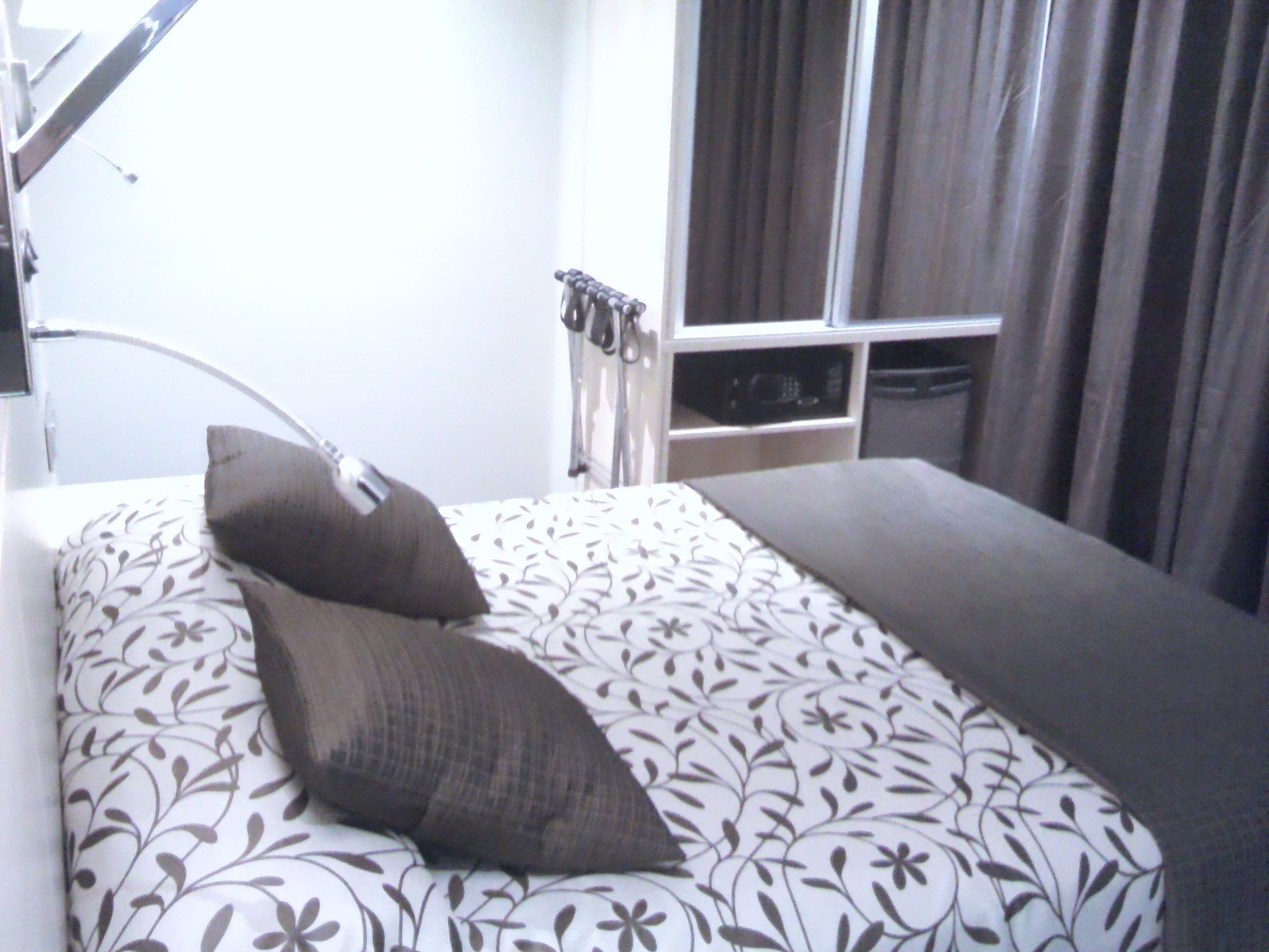 A bed with a floral-patterned bedspread and two pillows, a bedside table, and a window with curtains.
