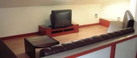 Un espacio habitable reducido con un televisor sobre un mueble bajo, una mesita y un sofá.