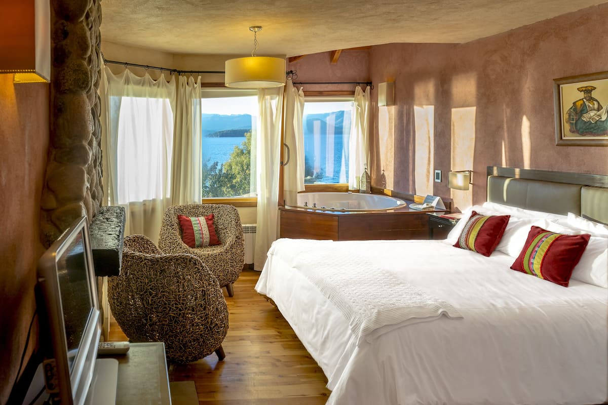 A hotel room with a large bed, a sitting area with a chair, a small table, and a view of a lake.