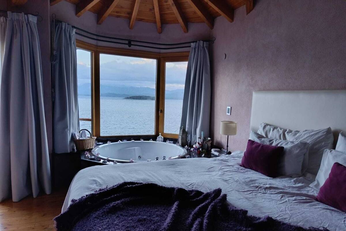 A bedroom with a large bed, a view of the sea through a window, and a bathtub.