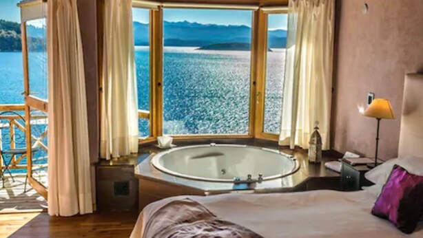 Quarto com uma cama grande, uma banheira e vista para um lago.