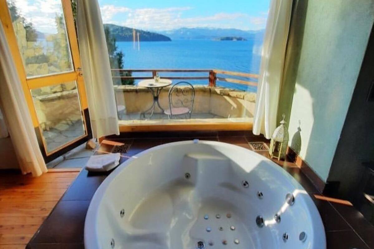 A room with a large bathtub, a view of the sea, and a balcony with a table and chairs.