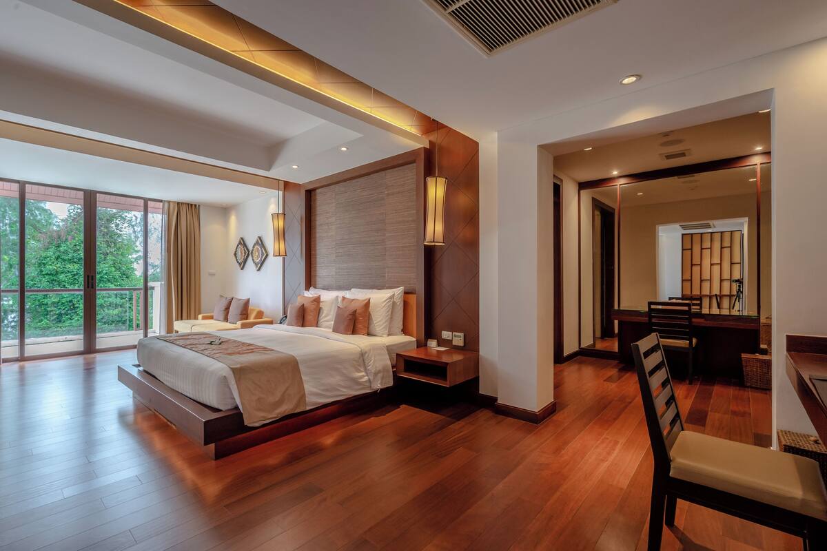 Een moderne slaapkamer met een groot bed, houten vloeren en uitzicht op groen door grote ramen.
