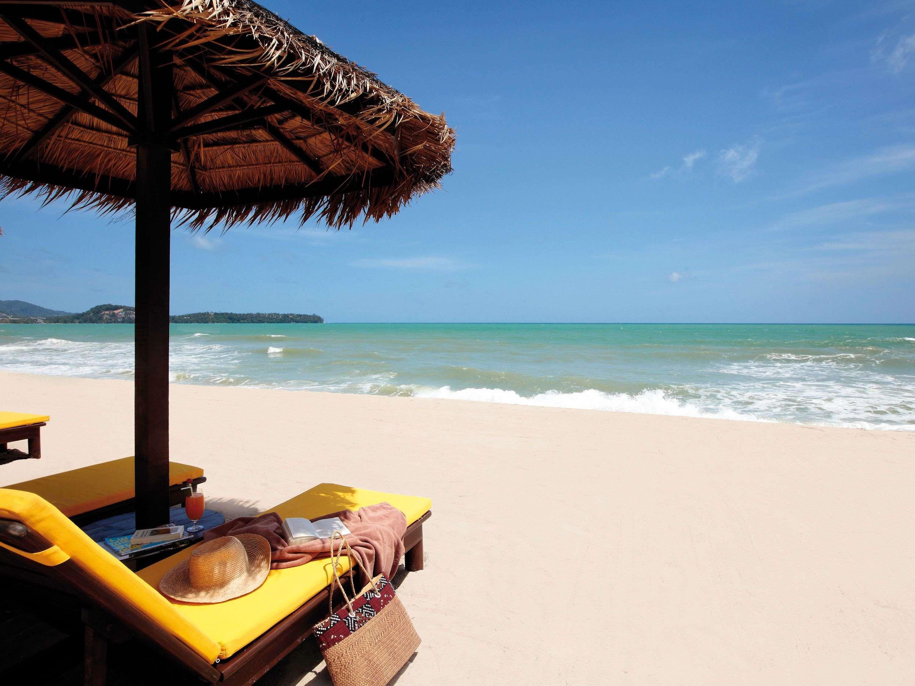 En strandscen med ett parasoll av halmtak, en gul solstol och en strandstol.