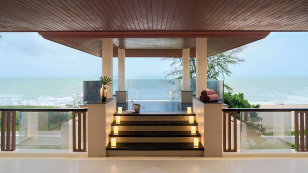 A balcony with a view of the ocean, featuring a wooden pergola, a glass railing, and a small table with candles and towels. - Mövenpick Phuket Bangtao (Choeng Thale)