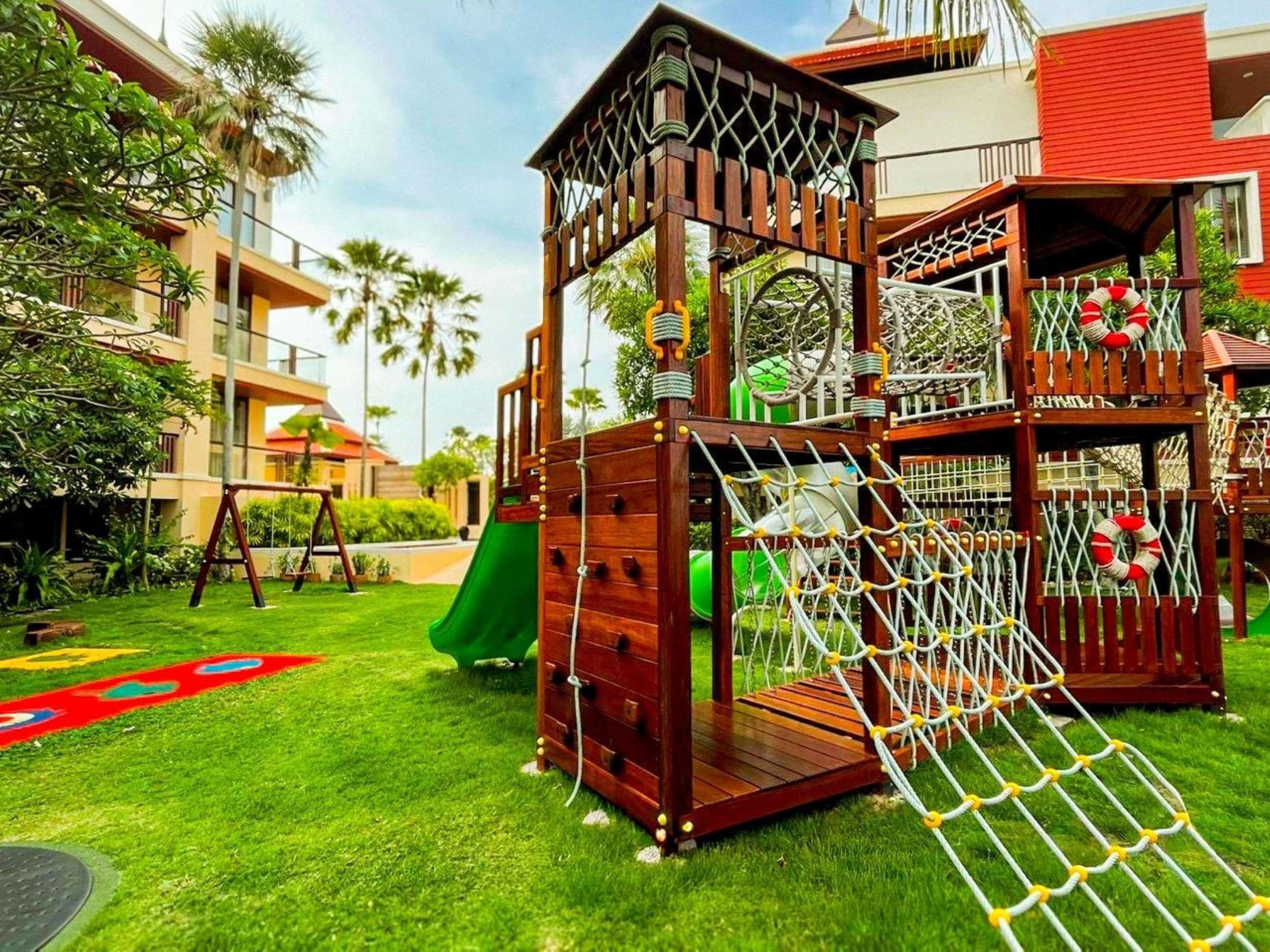 A playground with a slide, climbing net, and a wooden playhouse.