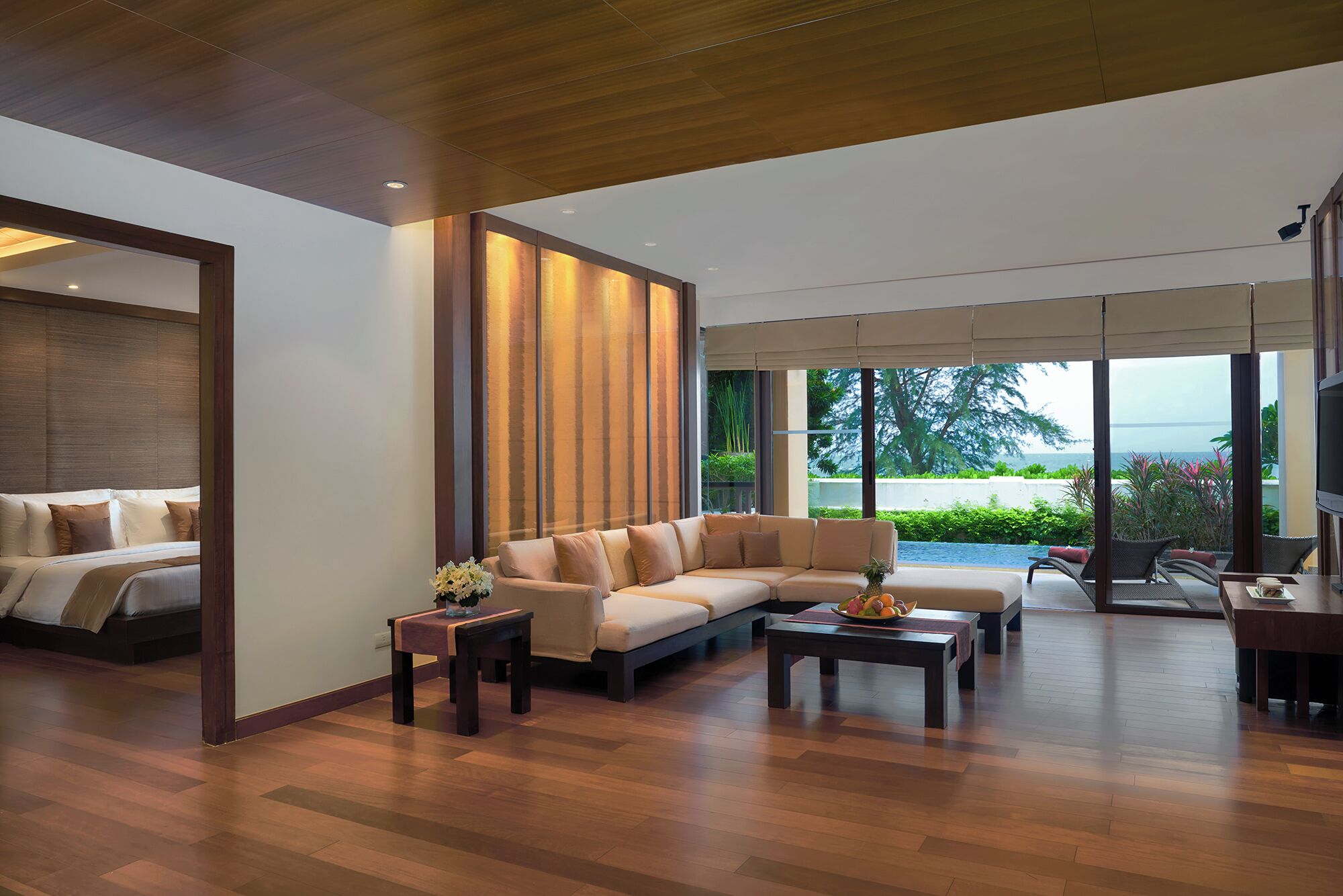 Una sala de estar moderna con un sofá modular, una mesa de centro y un televisor. Hay un ventanal con vistas a zonas verdes y un cuerpo de agua.