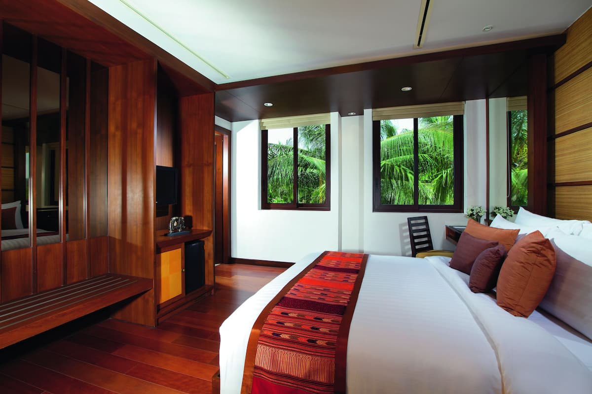 Een moderne hotelkamer met een groot bed, houten meubilair en grote ramen met uitzicht op groen.