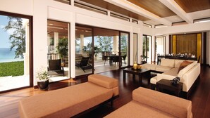 A spacious living area with a large sofa, a coffee table, and a dining table. There are large windows offering a view of the outdoors. - Mövenpick Phuket Bangtao (Choeng Thale)