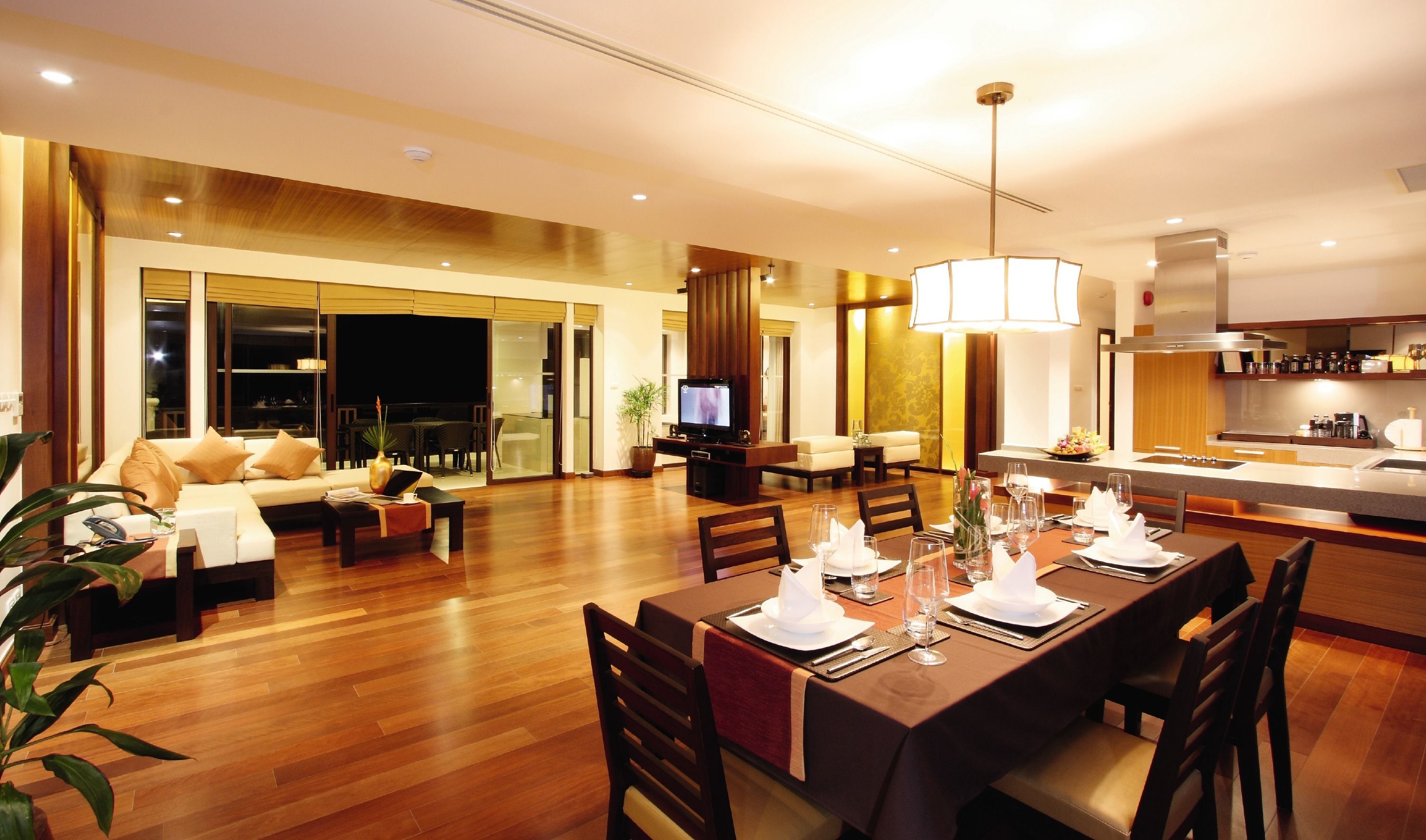 A modern hotel room with a dining area, a living room with a sofa and TV, and a kitchen area.