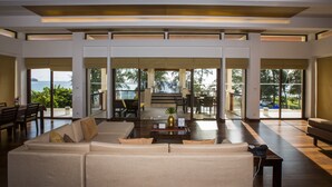A spacious living area with a large sofa, a coffee table, and a view of the ocean through large windows. - Mövenpick Phuket Bangtao (Choeng Thale)