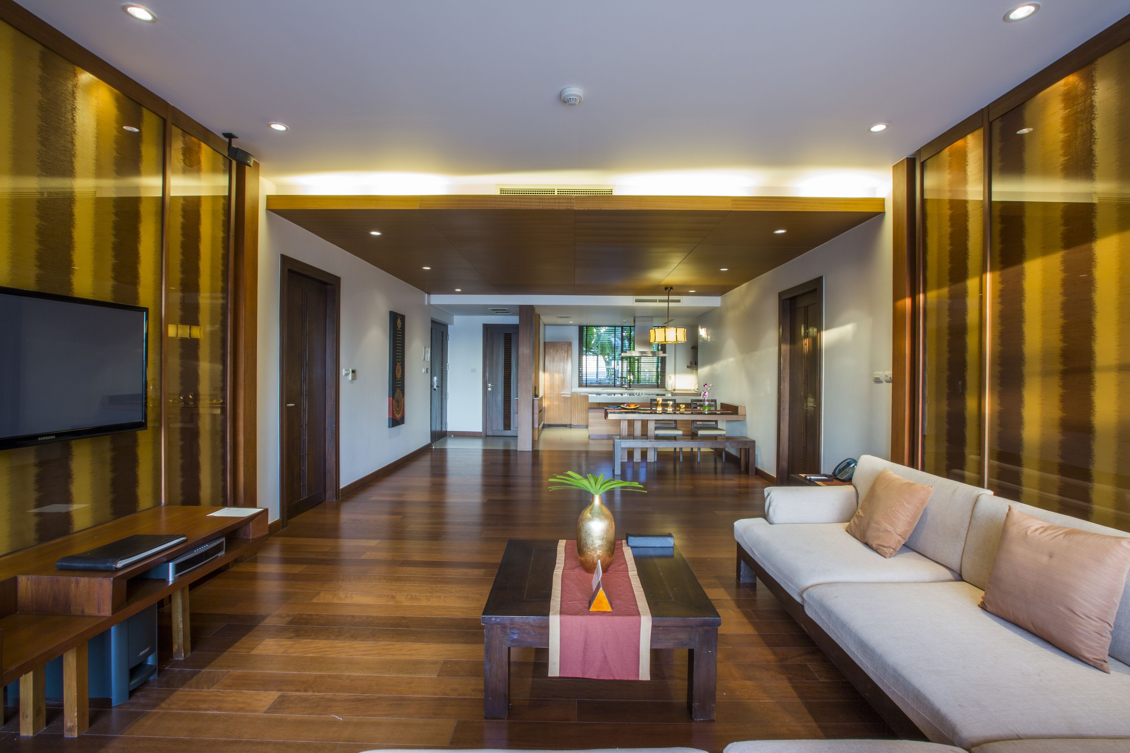 A spacious living area with a sofa, coffee table, and entertainment unit. A kitchen is visible in the background.
