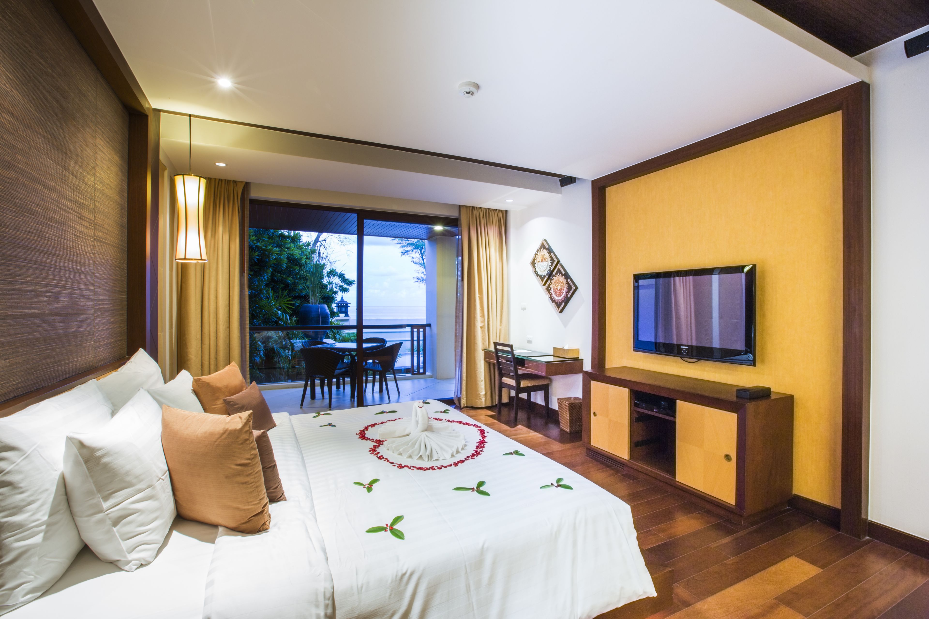 A hotel room with a bed, a TV, a dining area with a table and chairs, and a balcony with a view.
