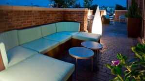 A brick patio with a light-colored sectional sofa and two round tables. - SpringHill Suites by Marriott Lafayette South at River Ranch (Lafayette)