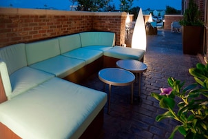Un patio de ladrillo con un sofá seccional de color claro y dos mesas redondas.