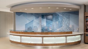 A reception area with a curved wooden counter, glass panels, and a large wall with text and geometric patterns. - SpringHill Suites by Marriott Lafayette South at River Ranch (Lafayette)