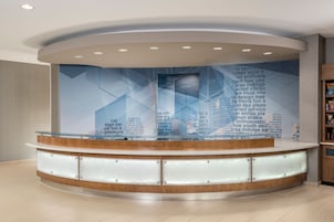 Un área de recepción con mostrador de madera curva, paneles de vidrio y una pared grande con texto y patrones geométricos.