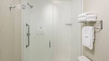 A modern bathroom with a glass-enclosed shower, a white toilet, and a towel rack with folded towels.