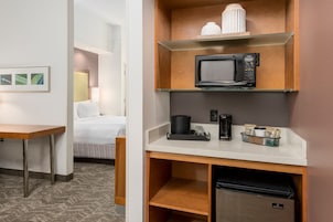 Una habitación de hotel con cama, escritorio, microondas, cafetera y refrigerador pequeño.