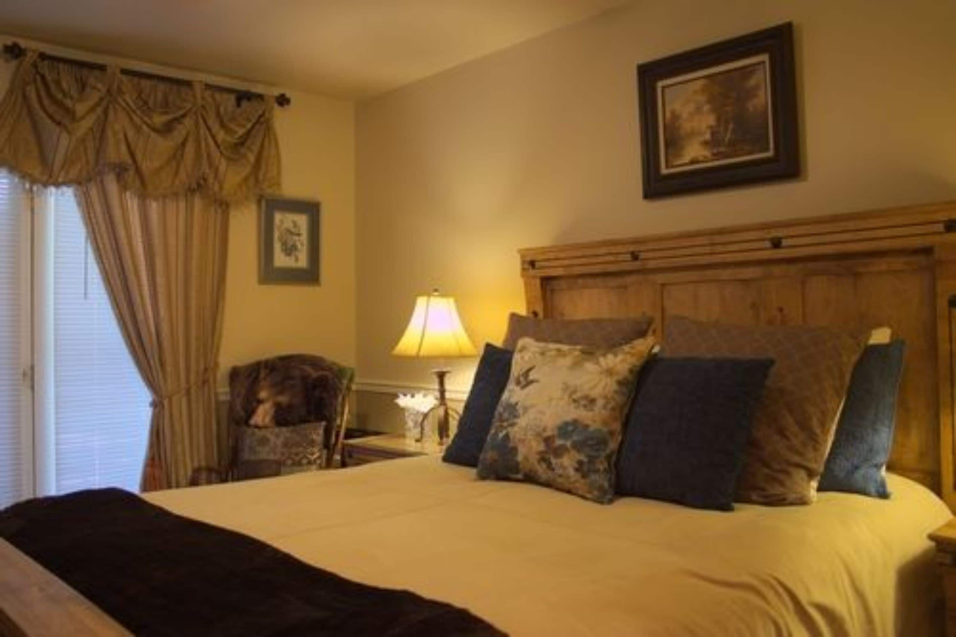 A bedroom with a large bed, a wooden headboard, a lamp, a chair, and a framed picture on the wall.