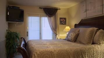 A bedroom with a bed, a television mounted on the wall, a ceiling fan, and a window with curtains.