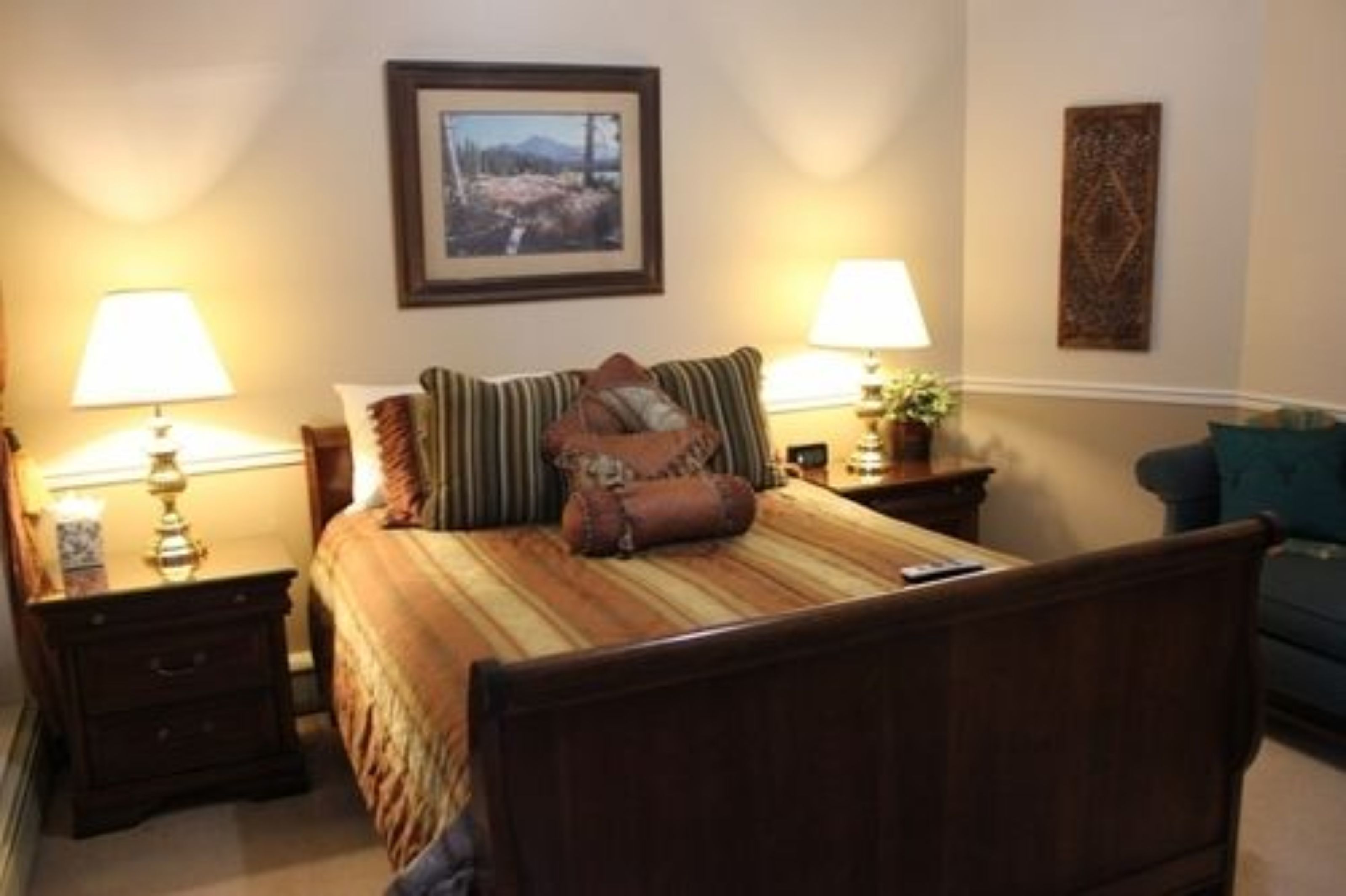 A neatly arranged bedroom with a bed, two bedside tables with lamps, a framed picture on the wall, and a small potted plant.