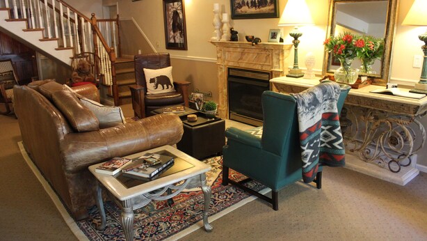 Ein Wohnzimmer mit braunem Ledersofa, einem Türkis-Sessel, einem Kamin und einer Treppe.