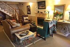 A living room with a brown leather sofa, a teal armchair, a fireplace, and a staircase. - Black Bear Manor (Ouray)