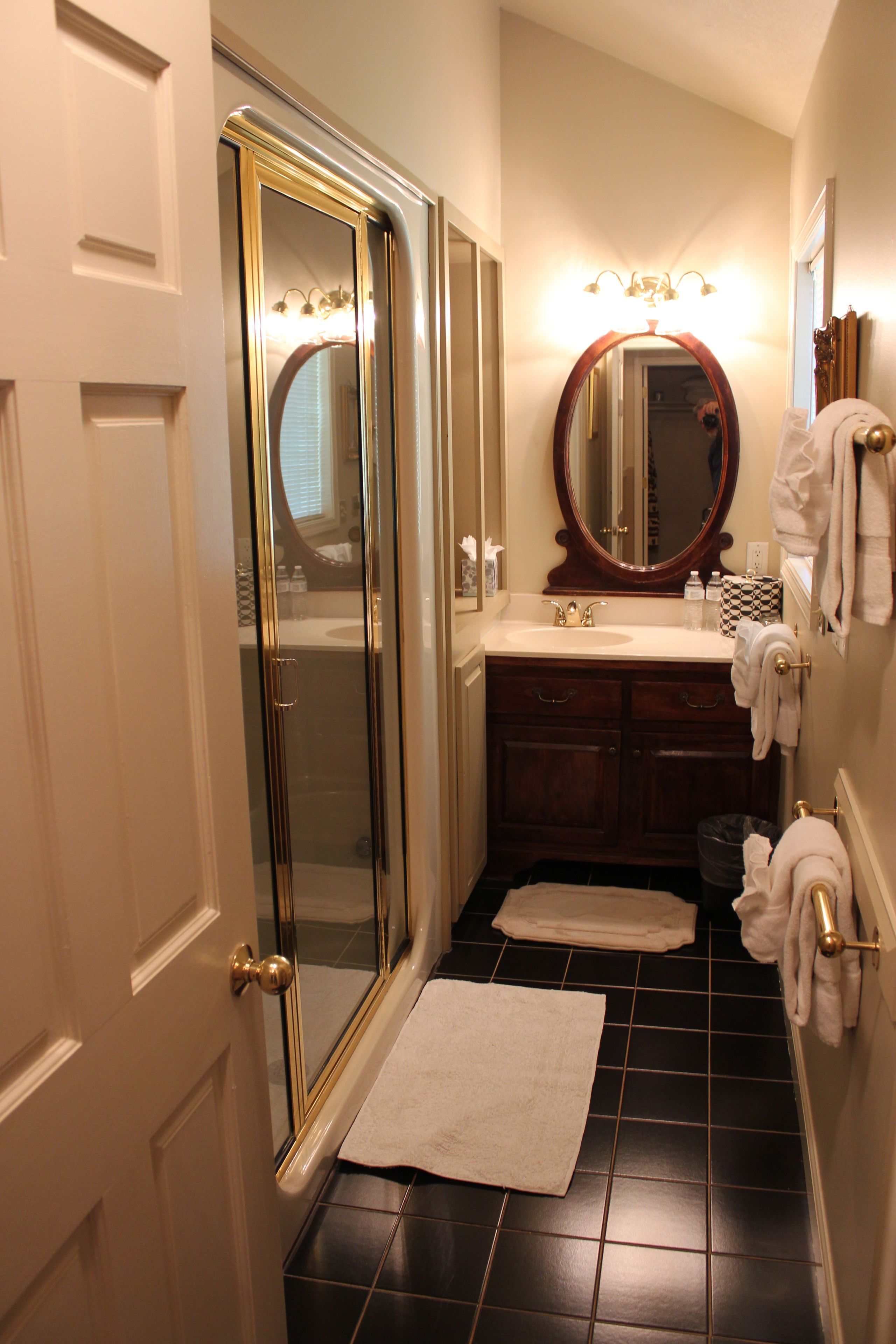 A bathroom with a glass-enclosed shower, a sink with a mirror above it, and a small rug on the floor.