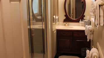 A bathroom with a glass-enclosed shower, a sink with a mirror above it, and a small rug on the floor.